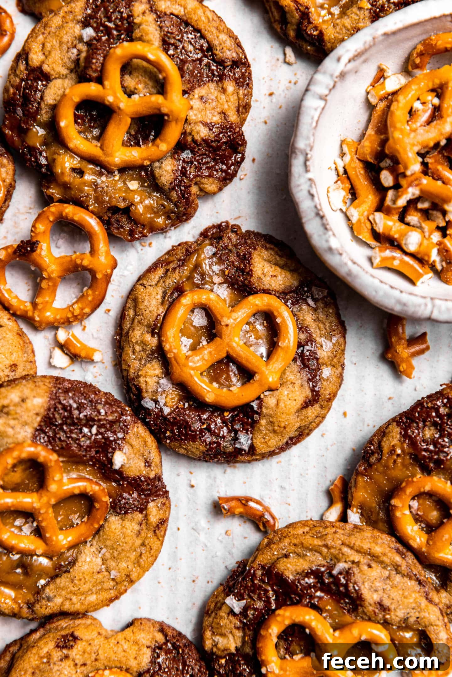 Close up of freshly baked Salted Caramel Pretzel Chocolate Chip Cookies on a baking sheet next to chopped pretzels.