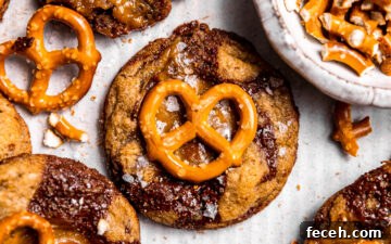 Close up of freshly baked Salted Caramel Pretzel Chocolate Chip Cookies on a baking sheet next to chopped pretzels.