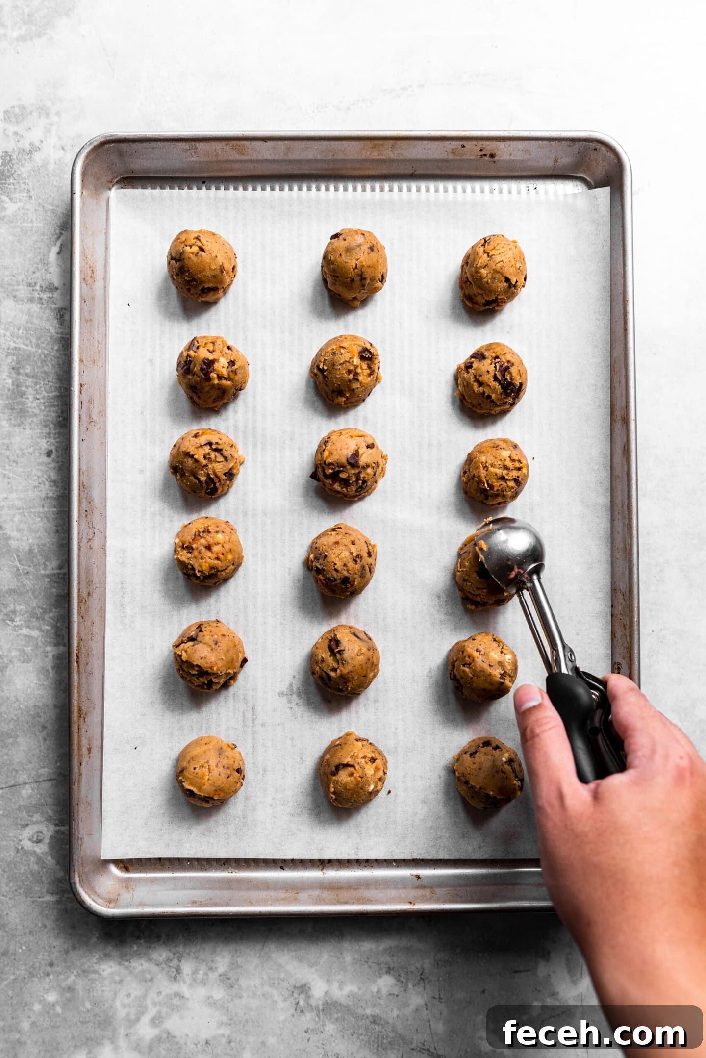 Cookie scoop dropping dough balls onto baking sheet.