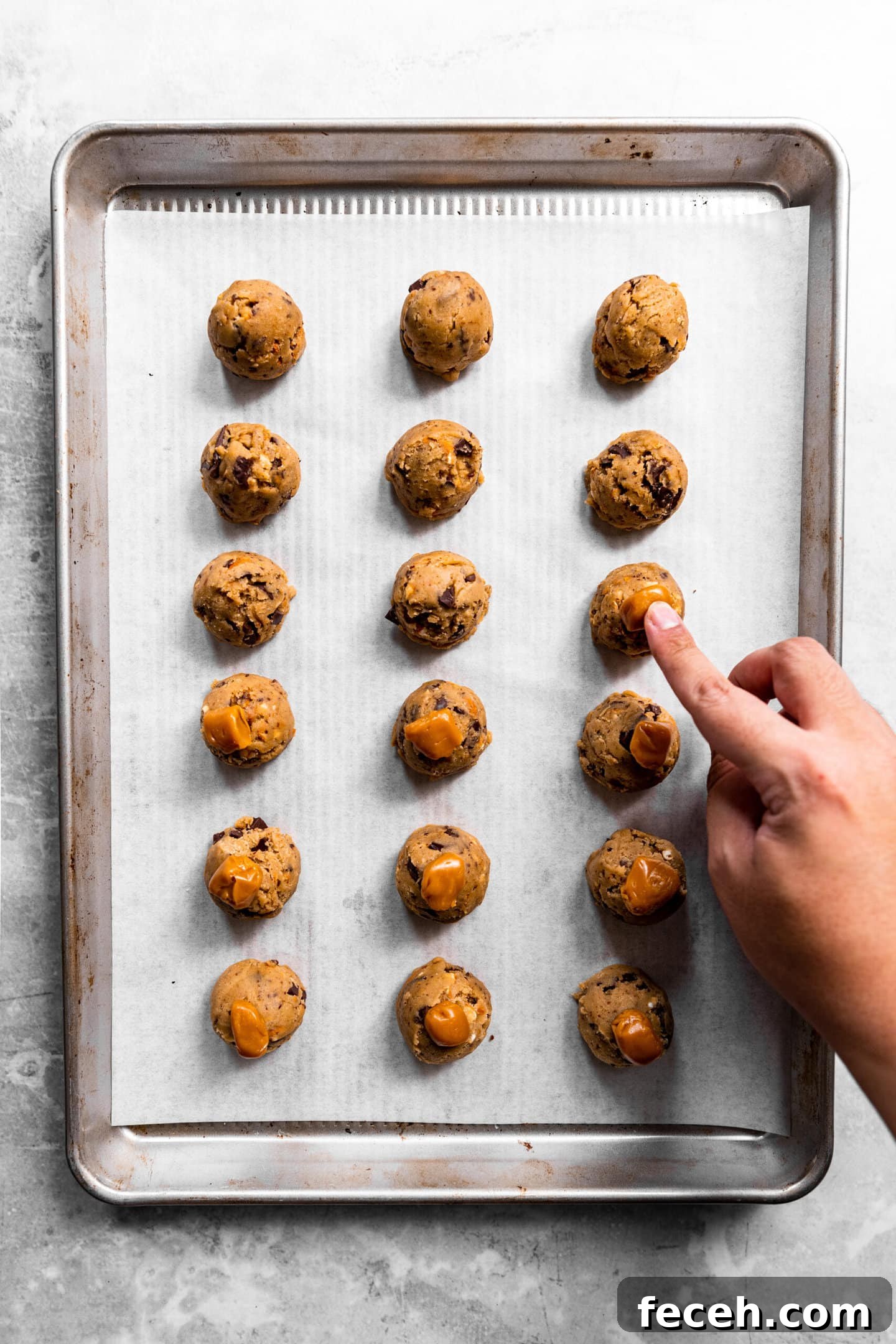Caramel chunks being pressed into the top of cookie dough balls.