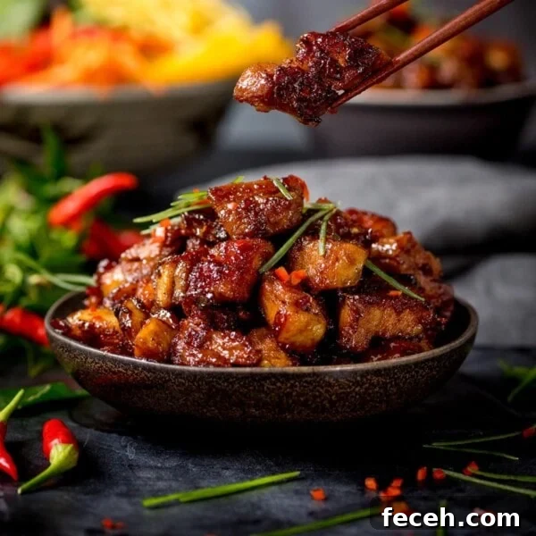 Close up image of bowl of Chinese sticky pork belly pieces. A piece is being taken from the bowl using a pair of chopsticks.