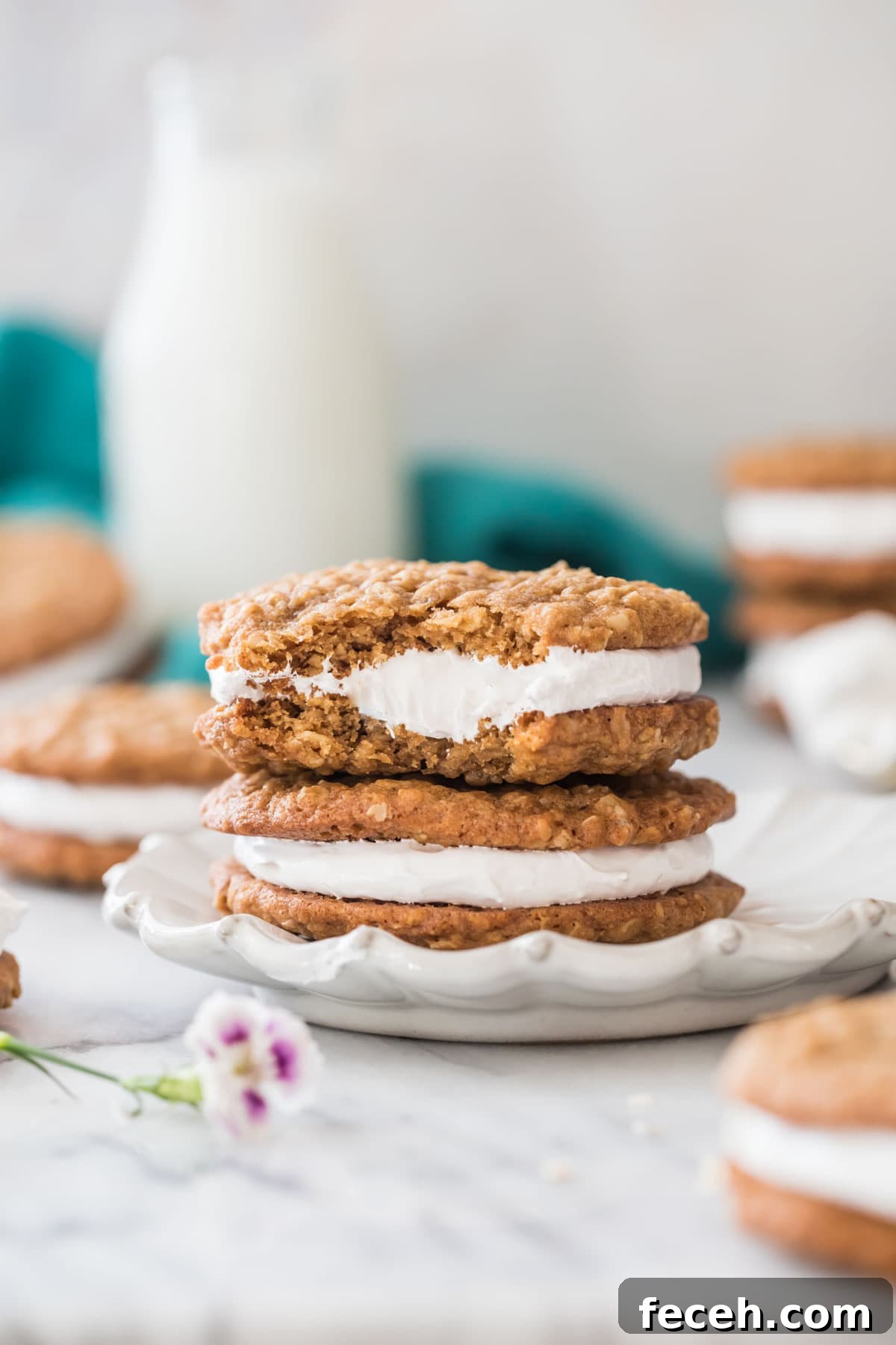 two oatmeal cream pies stacked on top of each other on a white decorative plate, with the top cream pie missing a bite