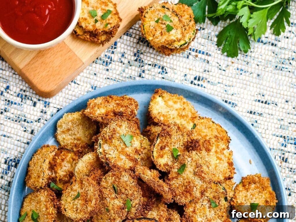 Breaded air fried zucchini chips on a blue plate with dipping sauce.