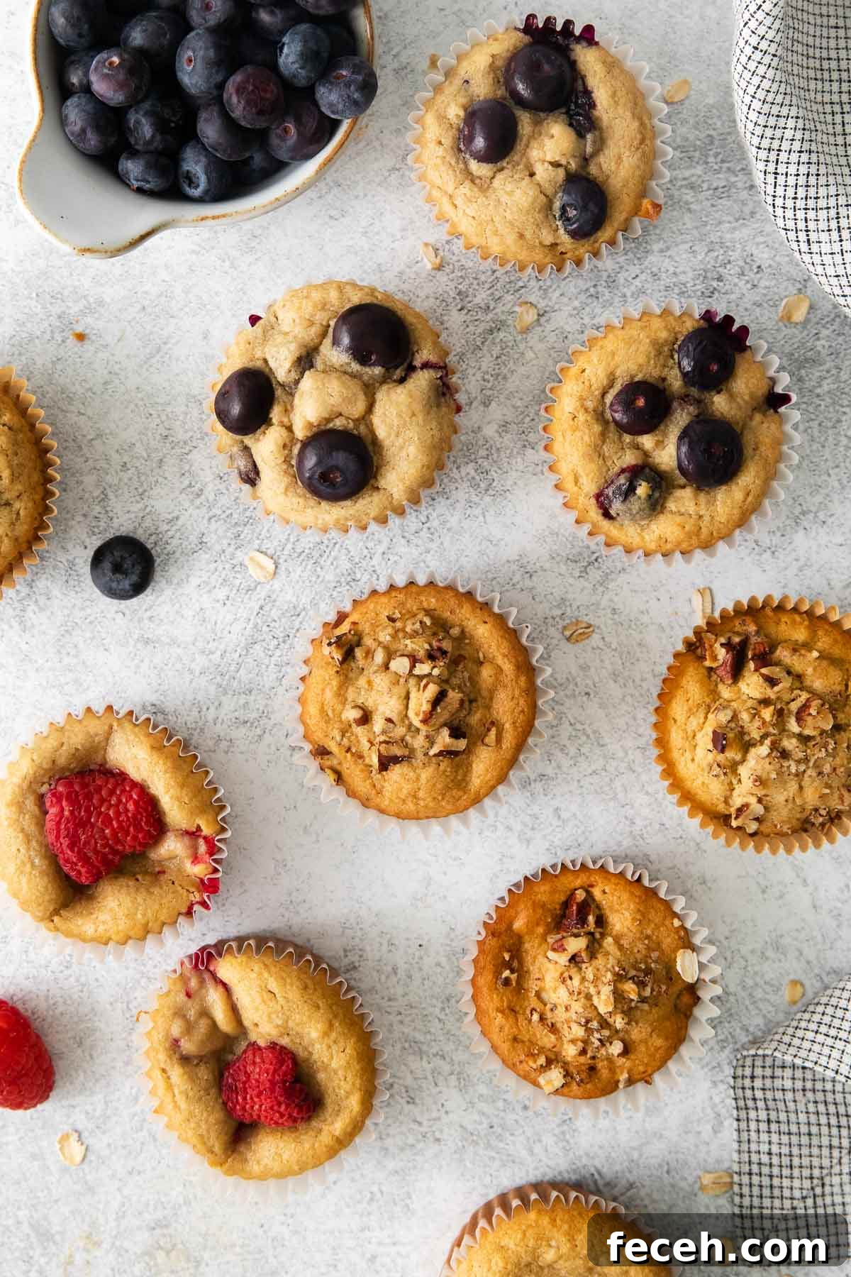 Oat flour muffins spread on a counter top with fruit around them