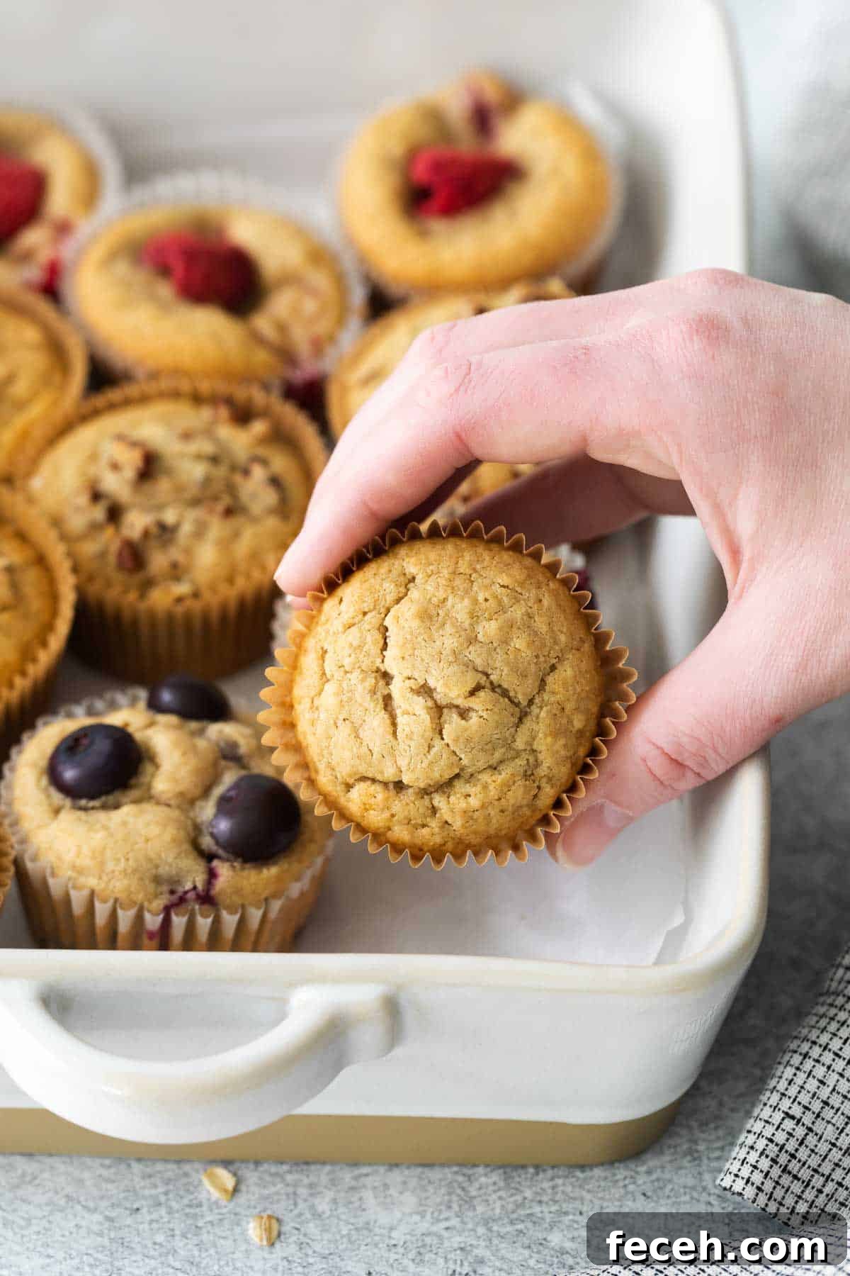 A hand reaching for a oat flour muffin in a baking dish