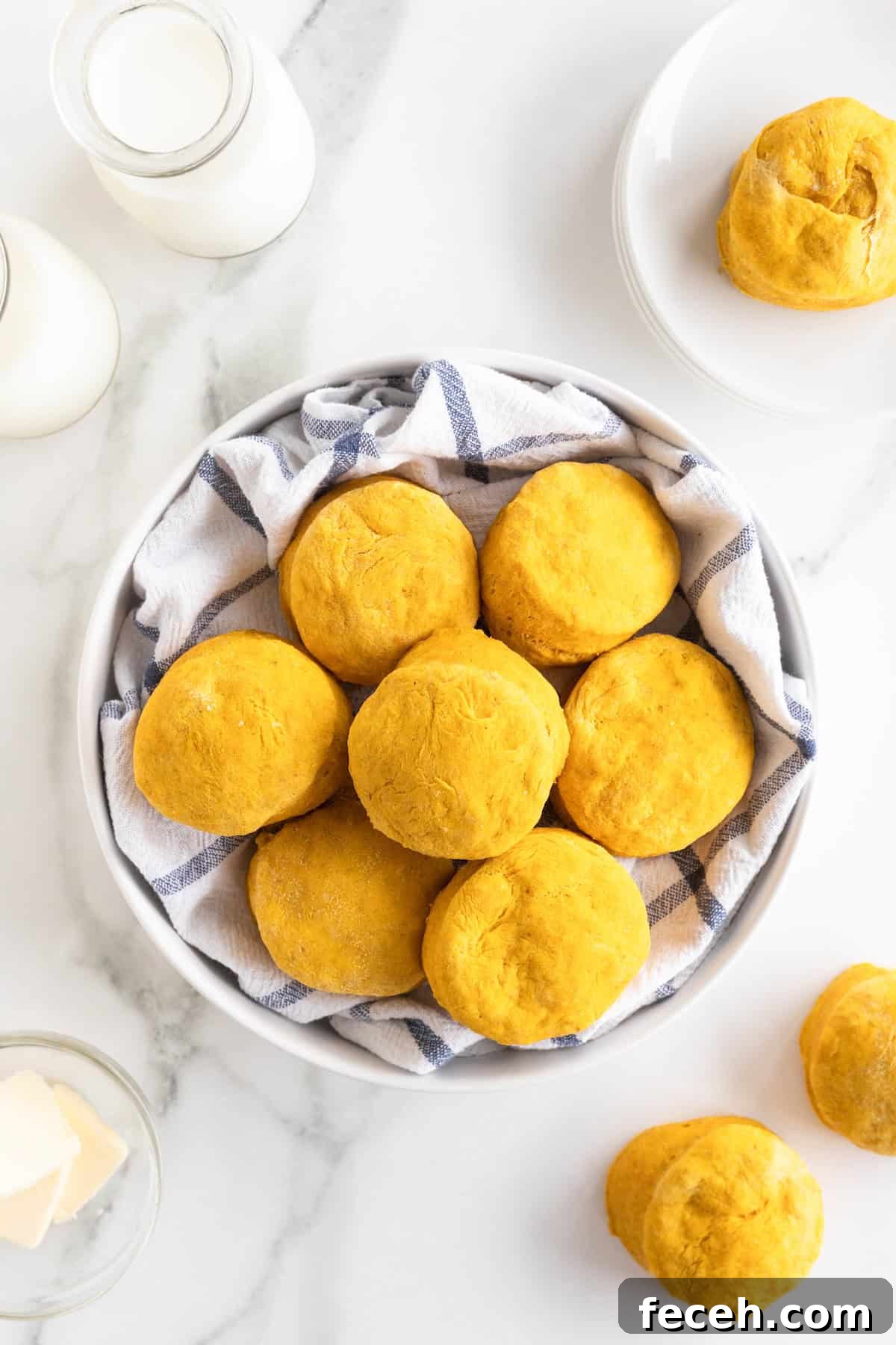 A large white serving bowl lined with a tea towel filled with pumpkin biscuits.
