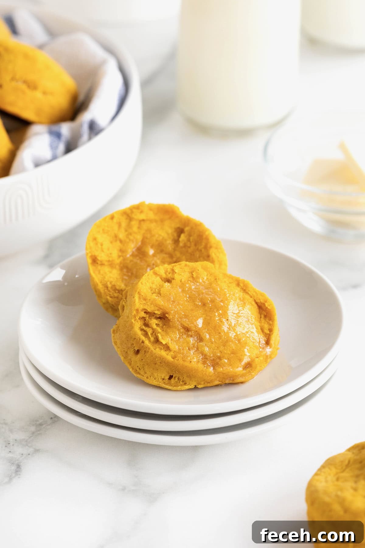 A pumpkin biscuit cut in half on a stack of three small white plates.