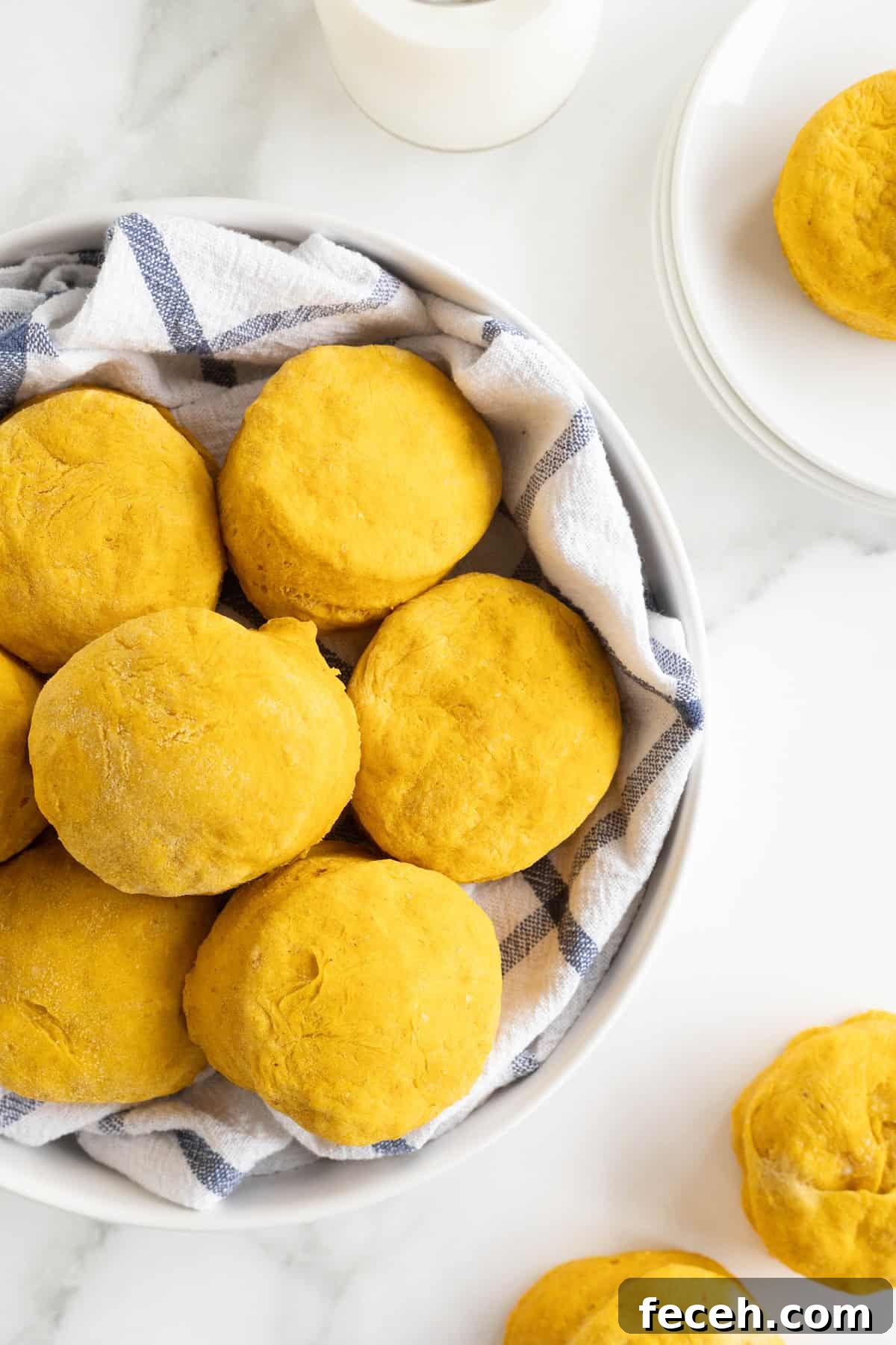 A large white serving bowl lined with a tea towel filled with pumpkin biscuits.