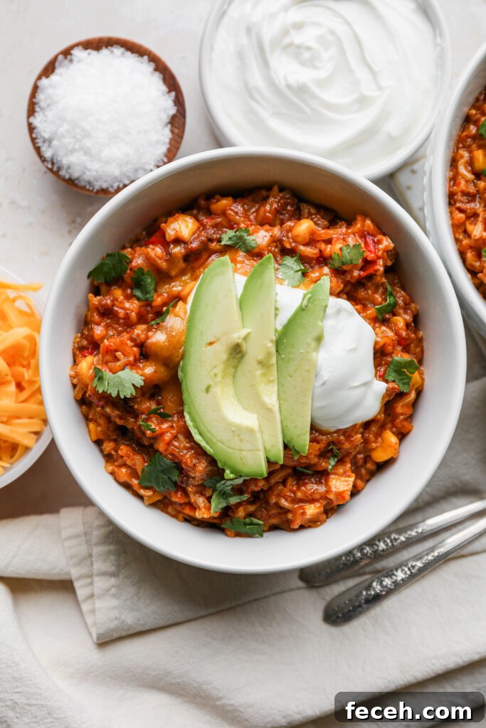 Instant Pot Mexican Beef and Rice Recipe for Flavorful Weeknight Meals 3 two white bowls of instant pot mexican style beef and rice next to a small white bowl of sour cream and a small white bowl of shredded cheddar cheese.