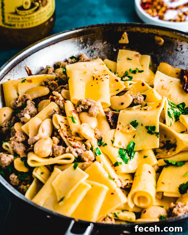 Paccheri Pasta With Butter Beans And Italian Sausage Angled shot of pasta in pan with chili flakes and olive oil in background.