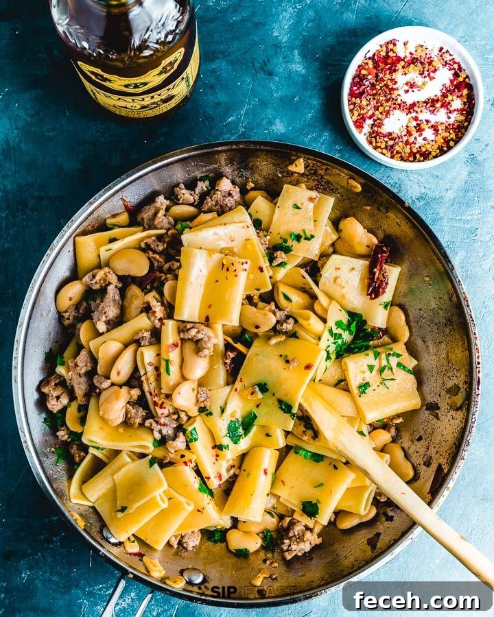 Paccheri Pasta With Butter Beans And Italian Sausage Overhead pic of pasta in pan, olive oil and small plate of chili flakes.