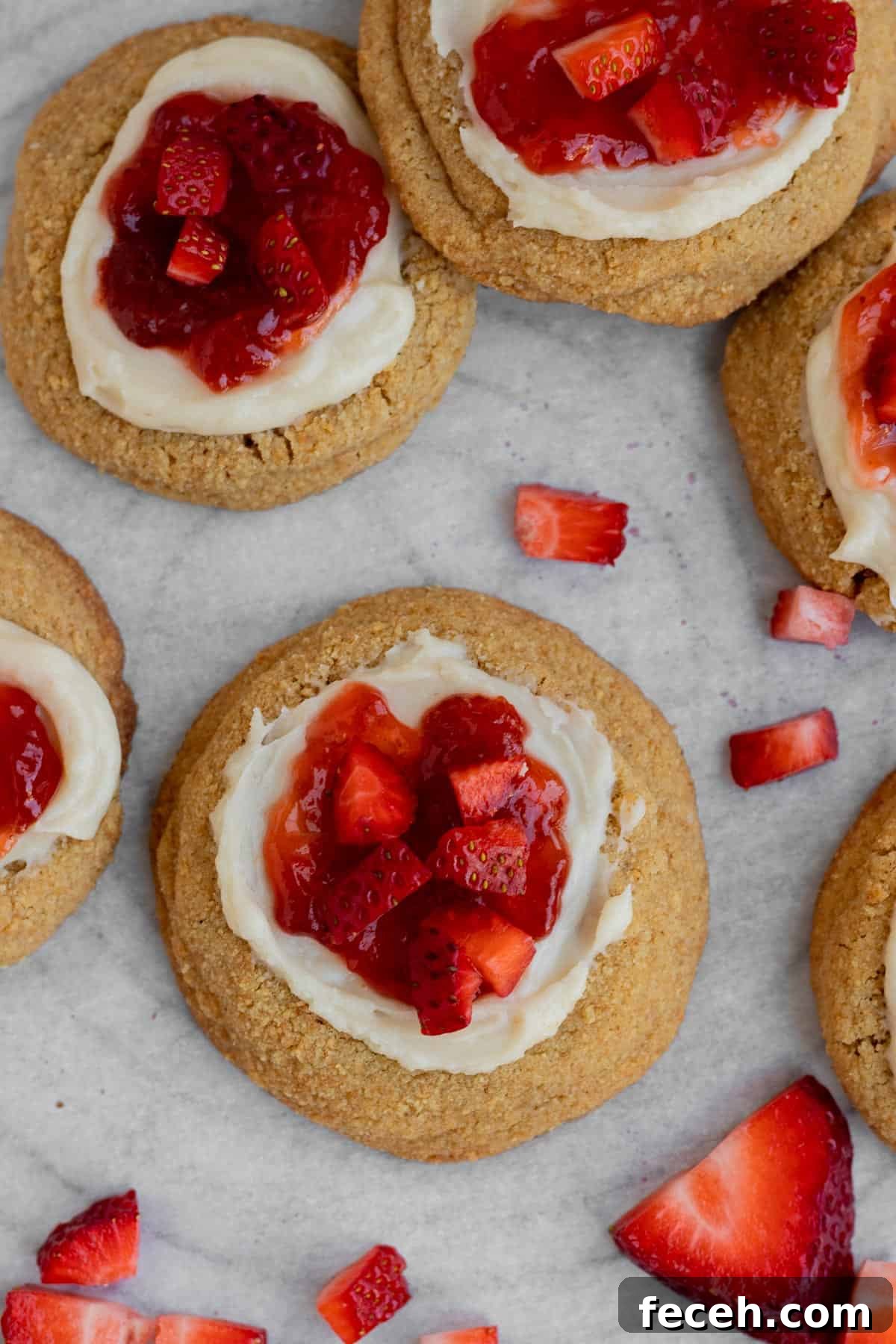 strawberry cheesecake cookies with cheesecake filling and strawberry jam with fresh strawberries sitting on parchment paper