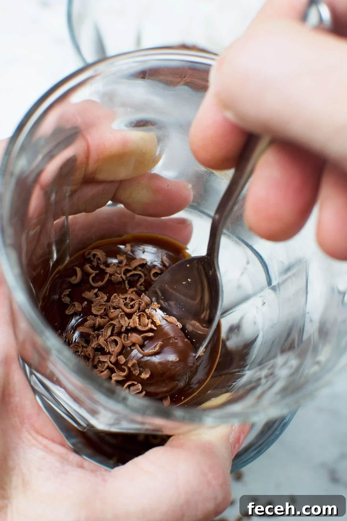 A closeup of someone holding a small glass and eating it with a spoon