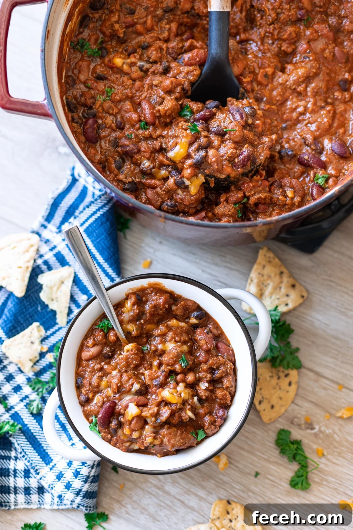 Hearty Three-Bean Chili Recipe: Simple Weeknight Dinner 3 Pot of chili in the background, close up on bowl topped with cheese and parsley.