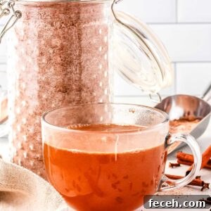 A jar of apple cider mix and then a teacup with spiced apple cider in it made with the mix.