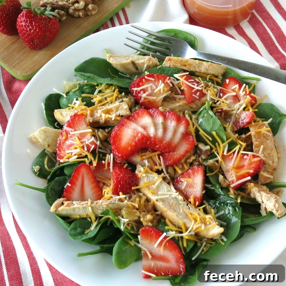 Spinach Strawberry Walnut Salad topped with chicken on a plate with walnuts and dressing in the background.