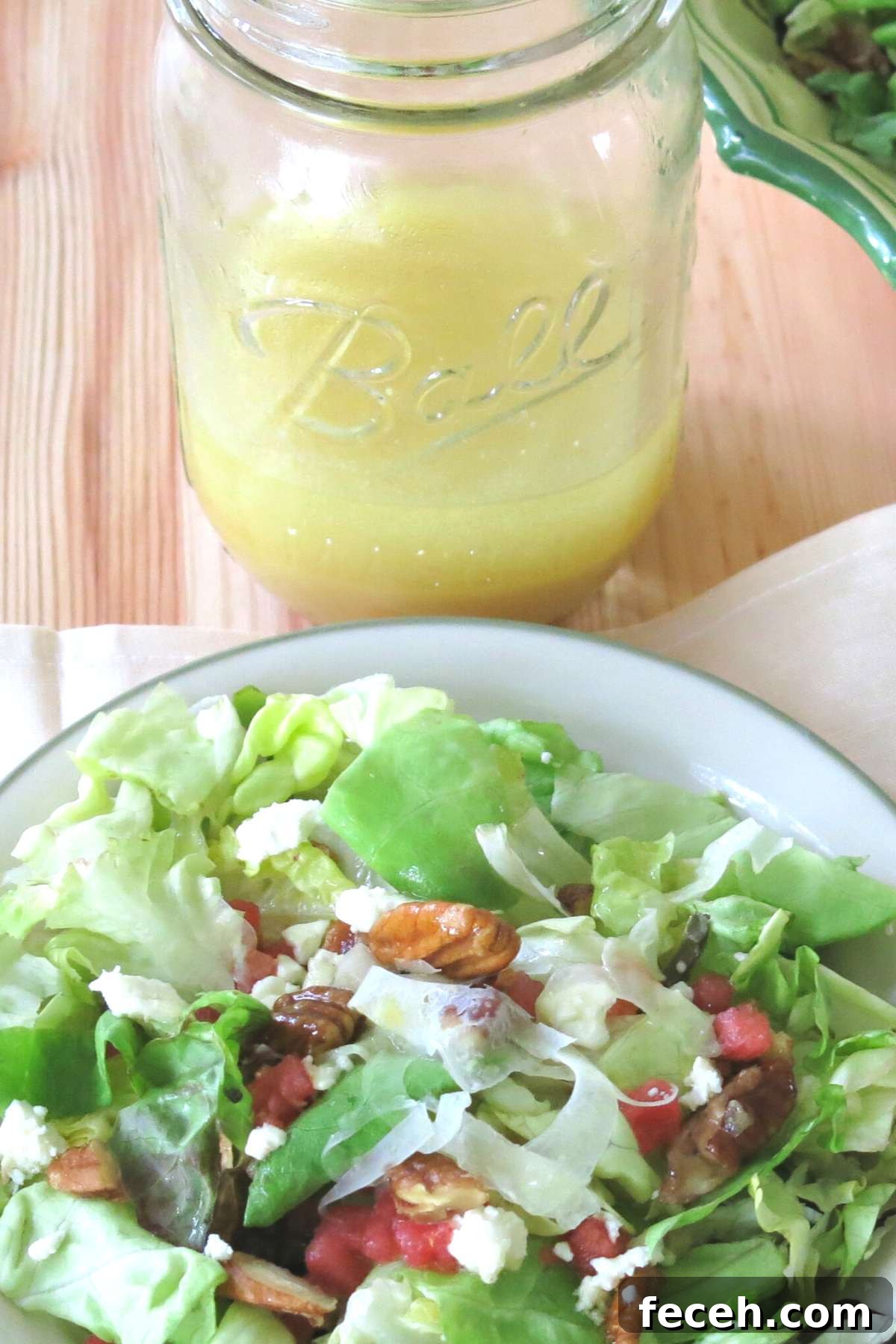 Summer Fennel Salad with Feta, Watermelon and Toasted Pecans 7 Orange honey mustard vinaigrette in a mason jar with a plate of summer salad with fennel, watermelon, feta, and candied pecans in front of it.