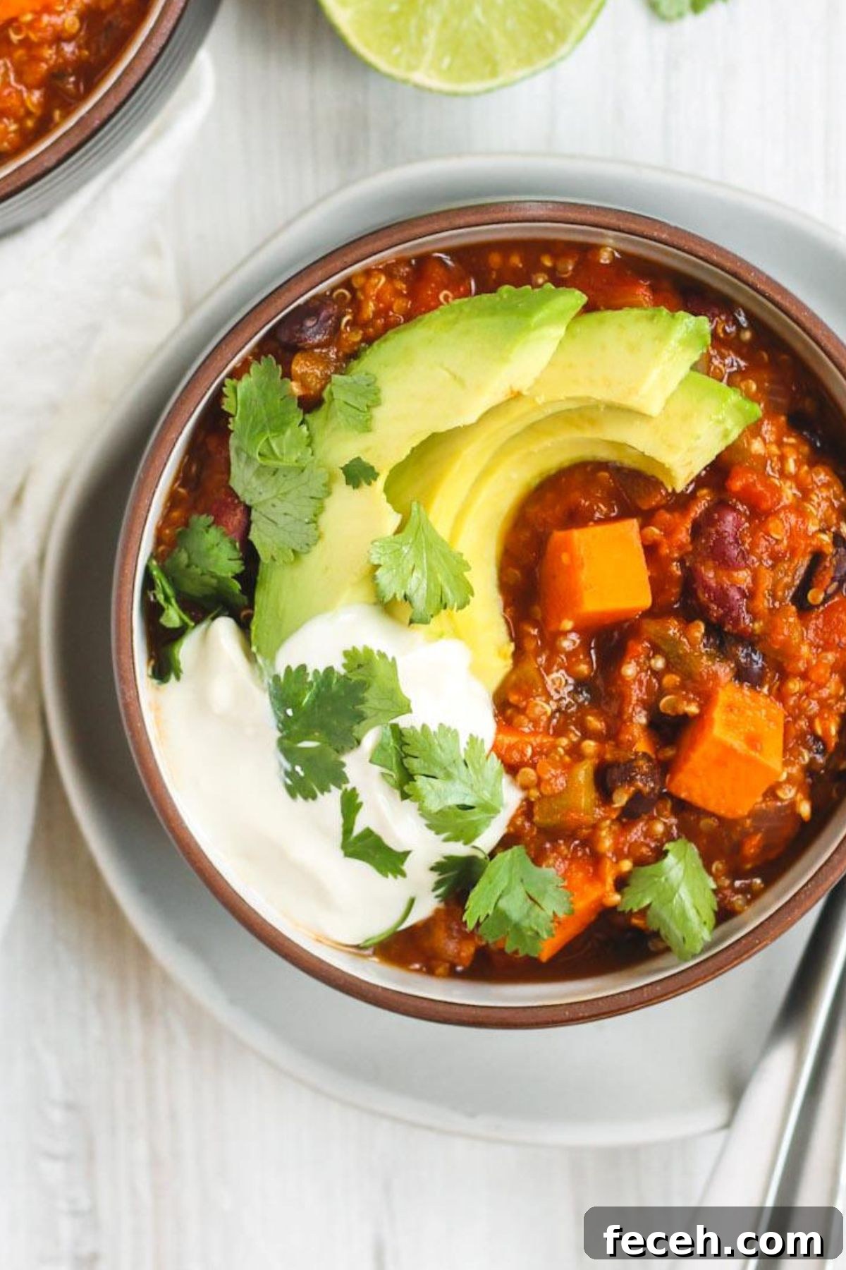 Vegetarian sweet potato topped with avocado, cilantro, and sour cream in a dark bowl sitting on a white plate.