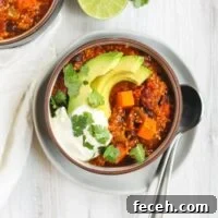 Vegetarian sweet potato topped with avocado, cilantro, and sour cream in a dark bowl sitting on a white plate.