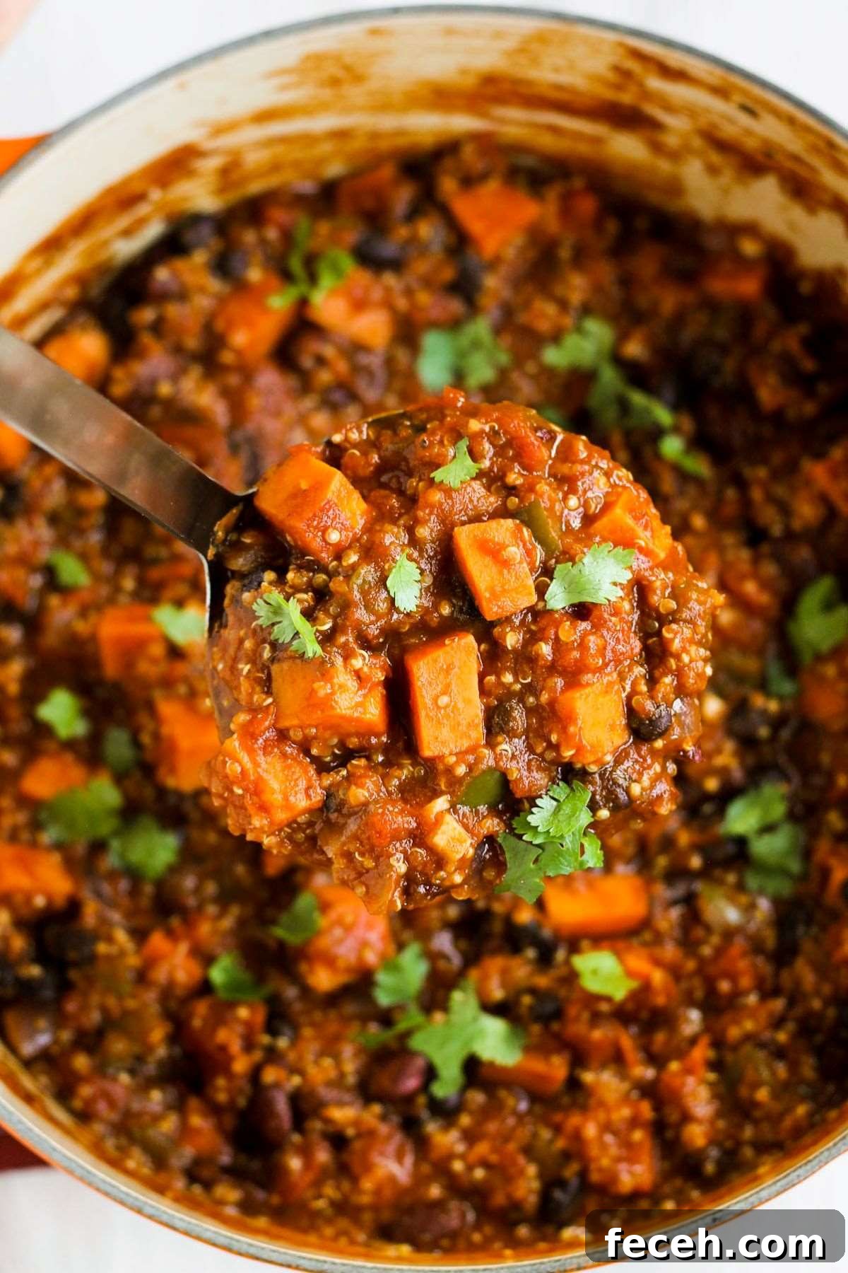 A stainless steel ladle scooping out a big scoop of sweet potato chili from a large stock pot.