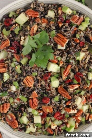 Wild rice salad with pecans, dried cranberries, and apples in a ceramic serving bowl with a vintage serving spoon in the salad.