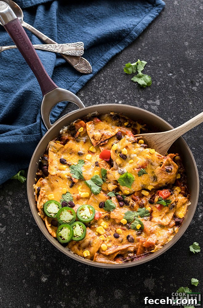One-Pot Veggie Enchiladas with Cheesy Sauce 4 one-pot vegetarian enchiladas in a skillet with a spatula and garnished with cilantro and jalapenos