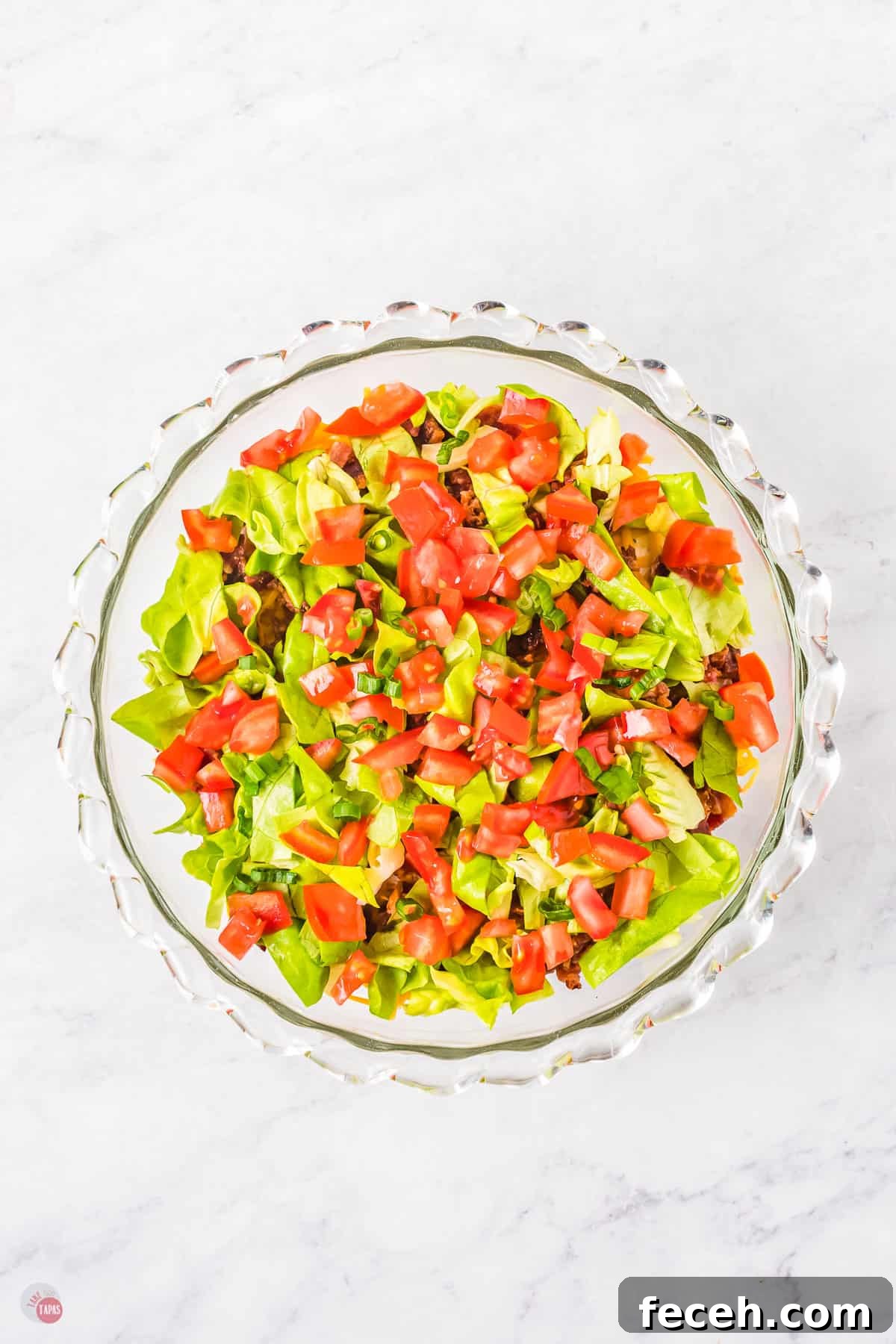 Glass bowl filled with mince with chopped tomatoes and chopped lettuce on top.