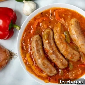 Sausage and Peppers in white serving dish next to peppers, garlic, and onions.