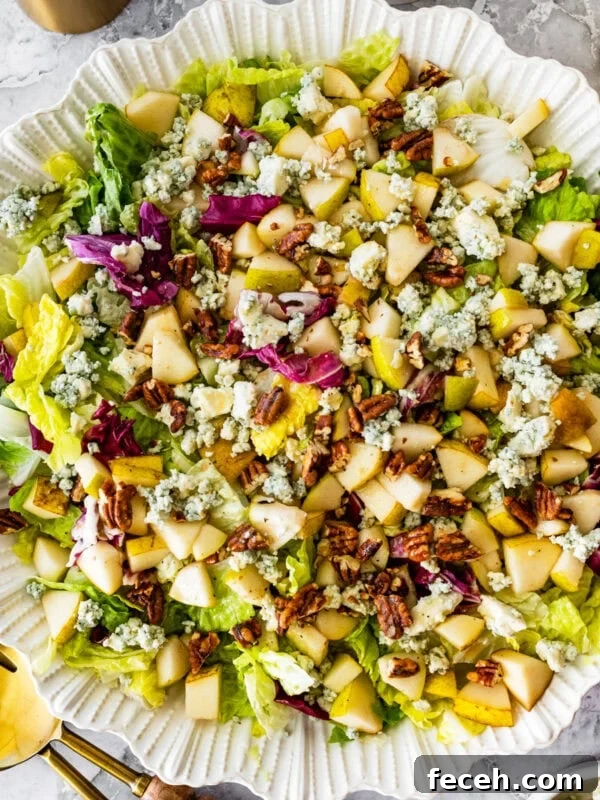 pear gorgonzola salad in a white serving bowl with salad servers near it.