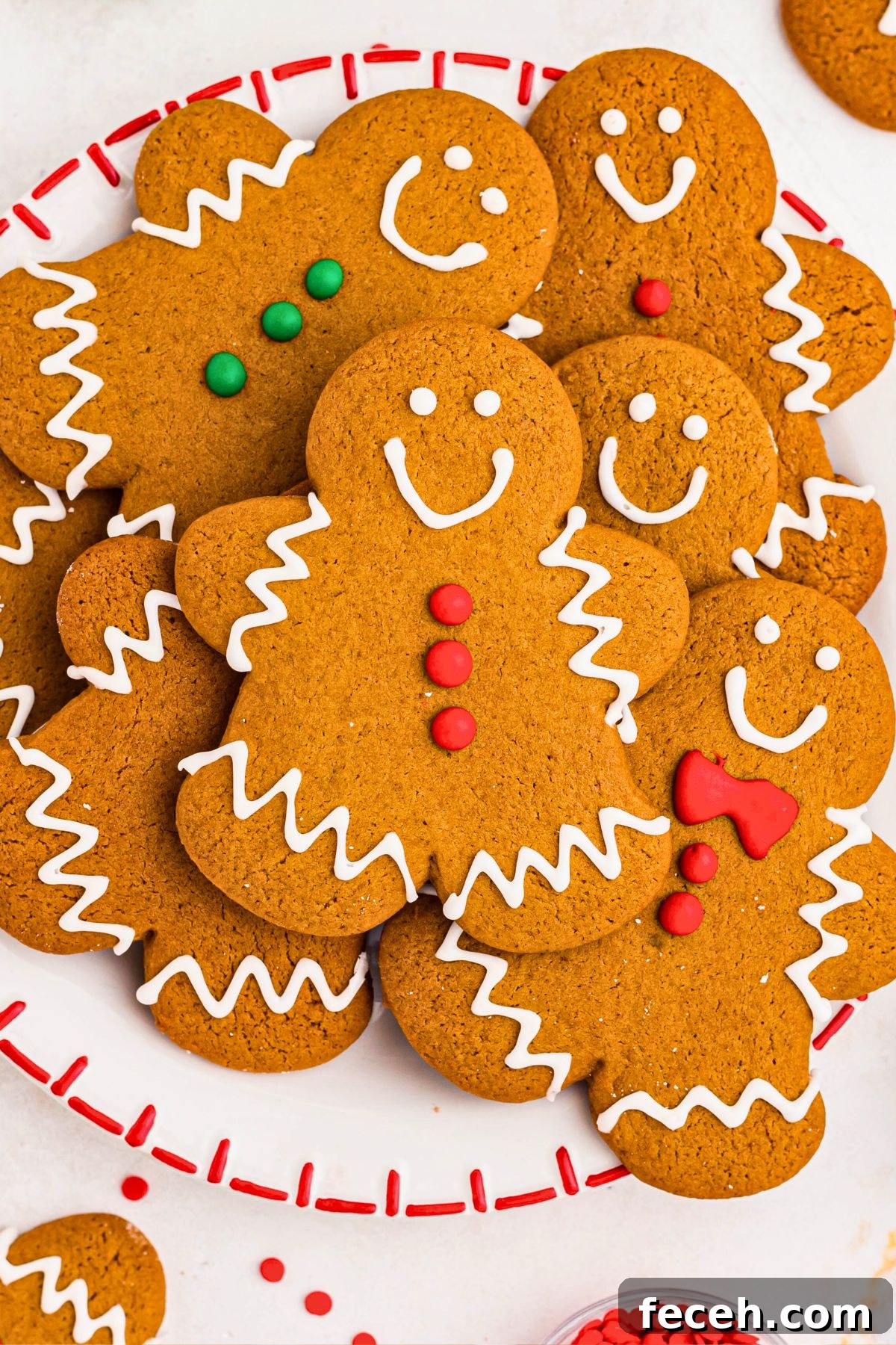 Classic Gingerbread Cookie Recipe for Soft, Spiced Cookies 11 Gingerbread cookies stacked on a white plate with sprinkles and other cookies scattered around the plate.