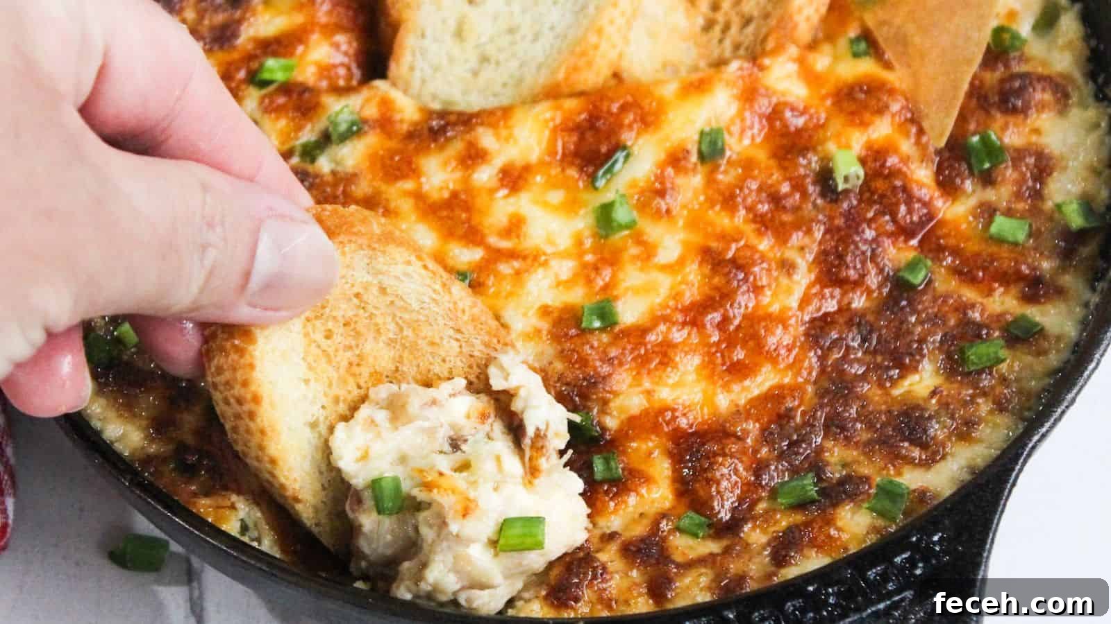 A person dipping a piece of bread into a skillet of cheesy dip.