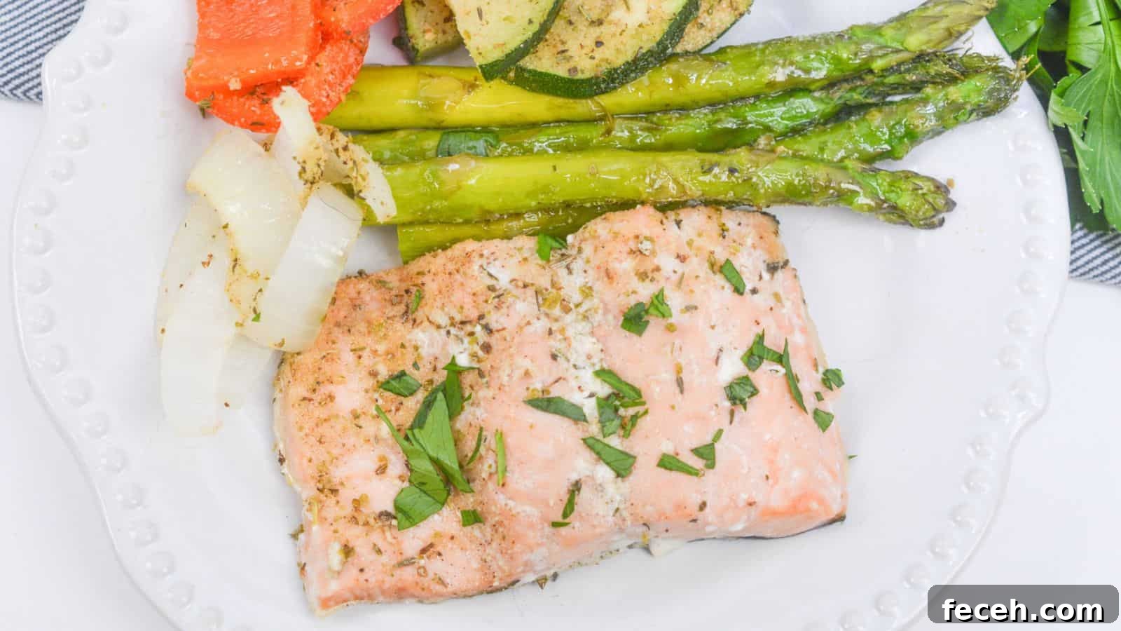 Baked salmon fillet with asparagus, zucchini, and bell peppers on a white plate, garnished with herbs.