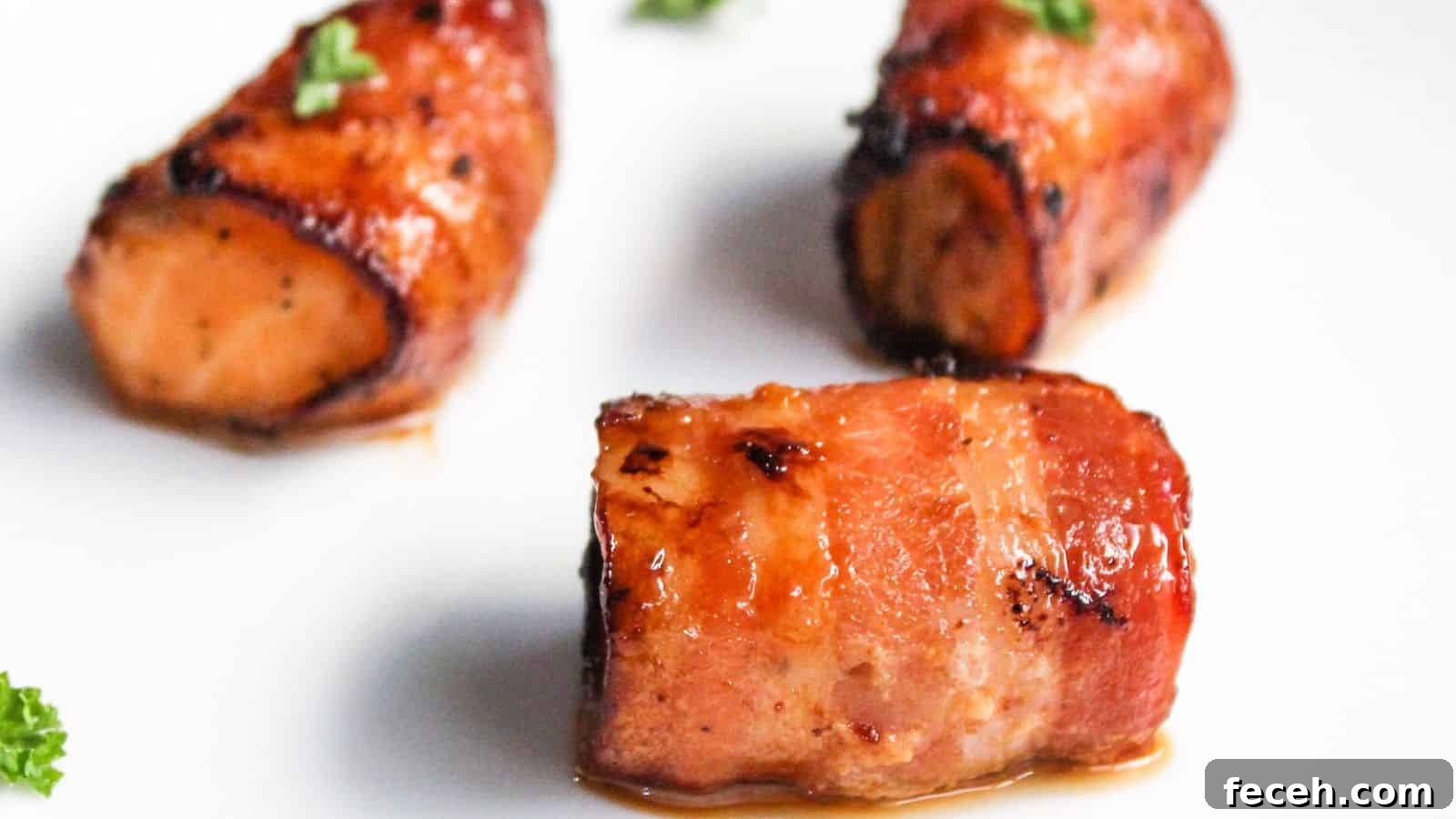 Three pieces of bacon-wrapped salmon bites garnished with parsley on a white plate.