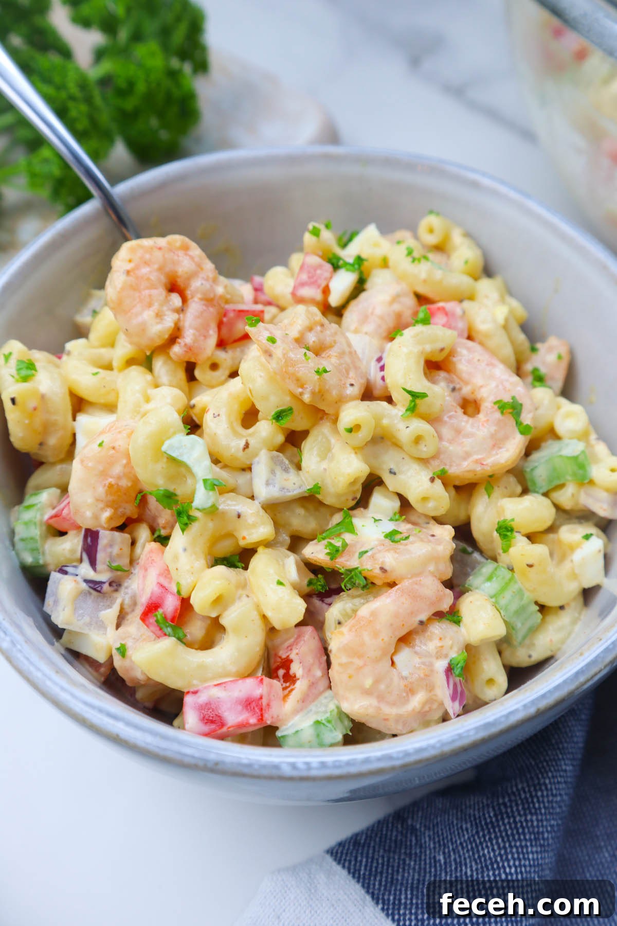 white bowl with macaroni salad tossed with old bay shrimp, red bell pepper, celery, topped with fresh parsley.