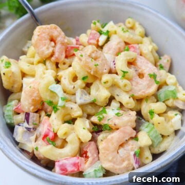 white bowl with macaroni salad tossed with old bay shrimp, red bell pepper, celery, topped with fresh parsley.