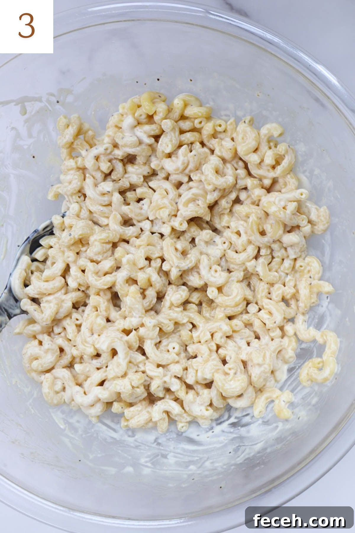 glass bowl with macaroni tossed in dressing.