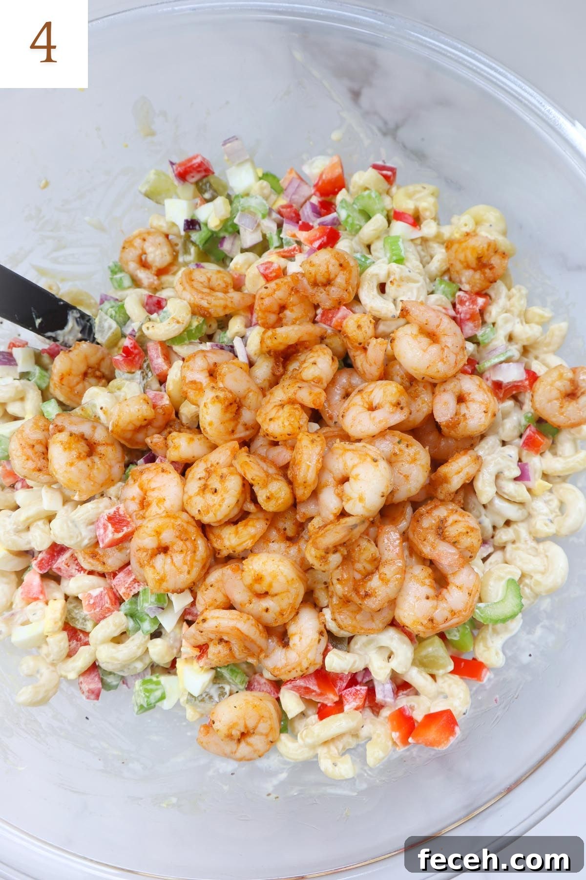 glass bowl with macaroni salad topped with veggies and old bay cooked shrimp.