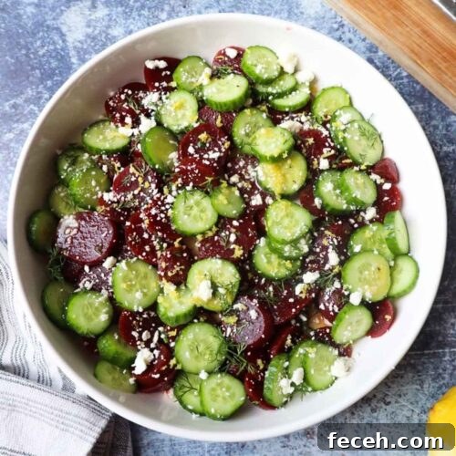 white bowl with beet and cucumber salad topped with a lemon dressing, lemon zest, and feta cheese