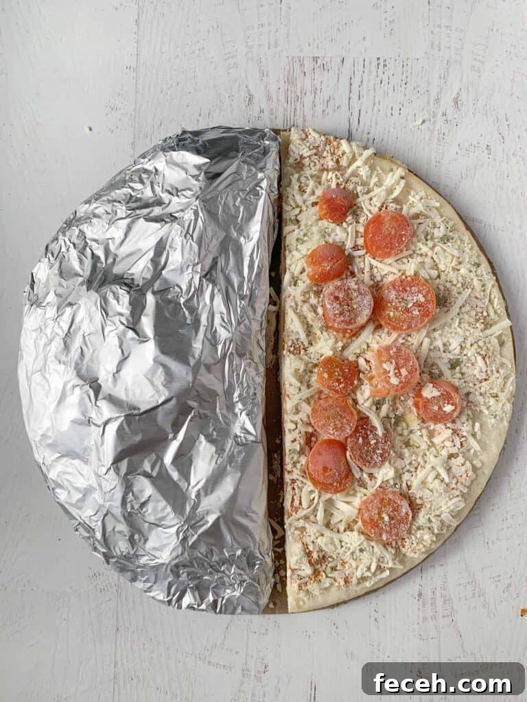 A frozen margarita pizza cut in half, half is wrapped in foil.