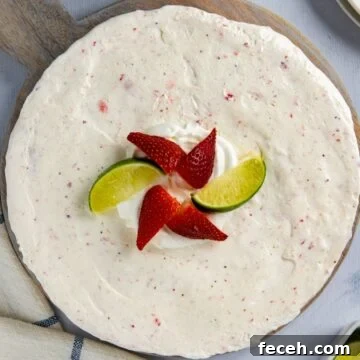 Whole pie topped with strawberry and lime wedges on a round wooden board.