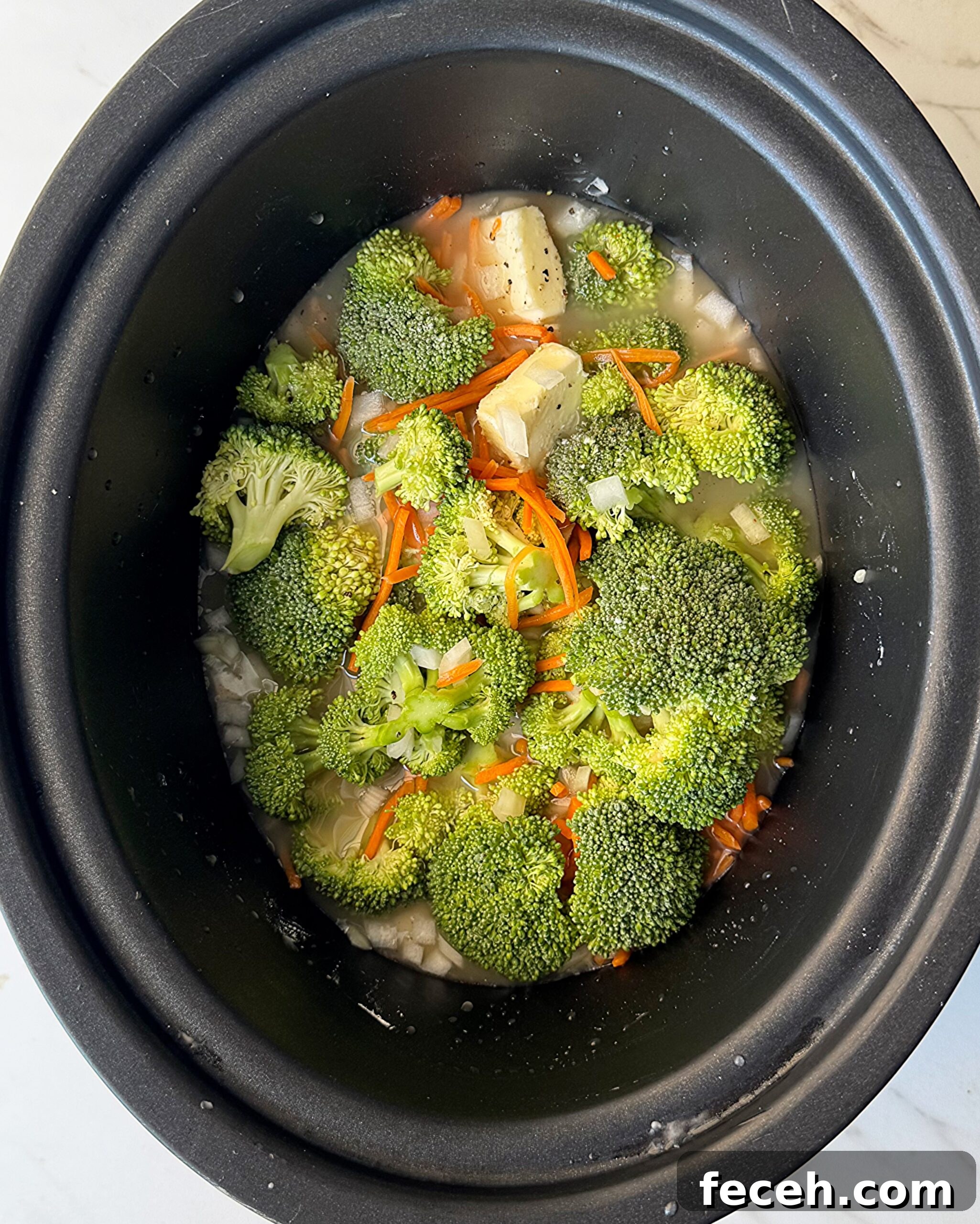 overhead shot of uncooked Broccoli Cheddar Soup in a black slow cooker