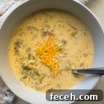 overhead shot of Broccoli Cheddar Soup in a white bowl garnished with cheddar cheese with a silver spoon