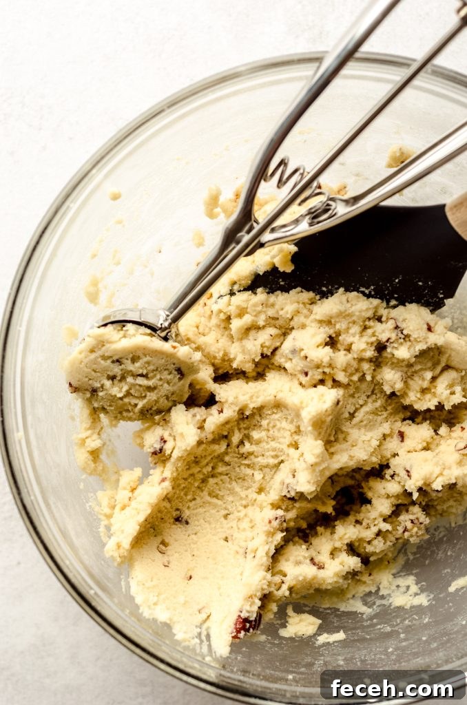 Goat cheese sugar cookie dough in a large glass bowl with a cookie scoop and spatula in the bowl.