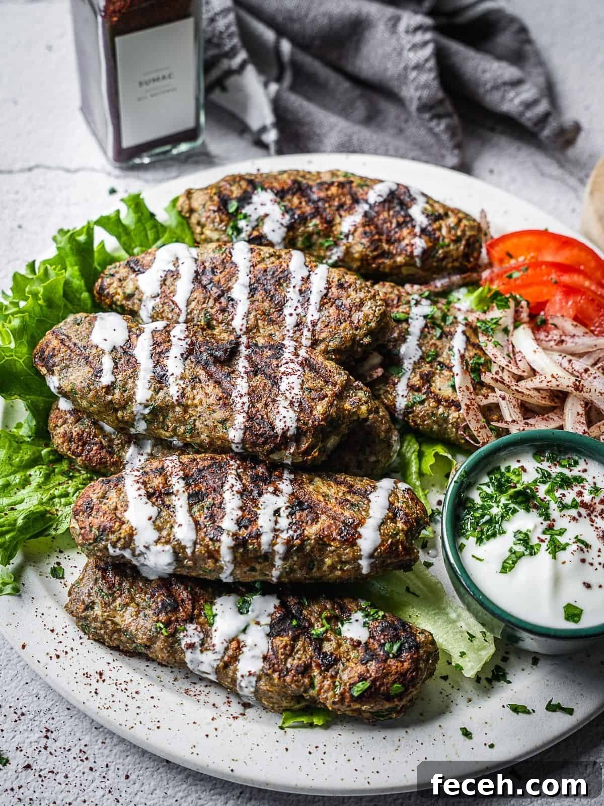 chicken kafta pieces on a plate with yogurt sauce, tomatoes and onions.