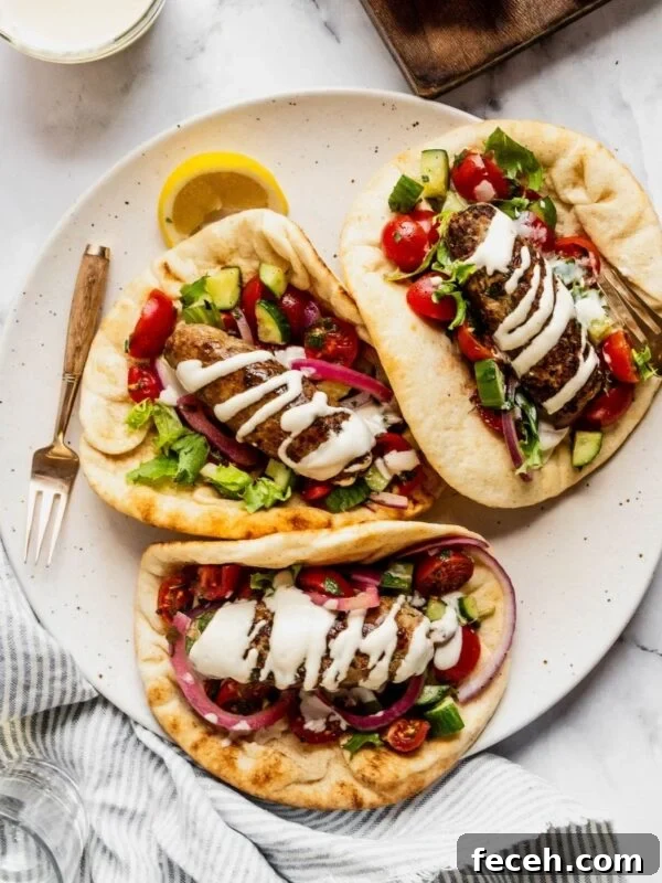 Plate with three turkey kofta wraps garnished with tahini sauce, pickled onions and chopped salad with cherry tomatoes and cucumbers.