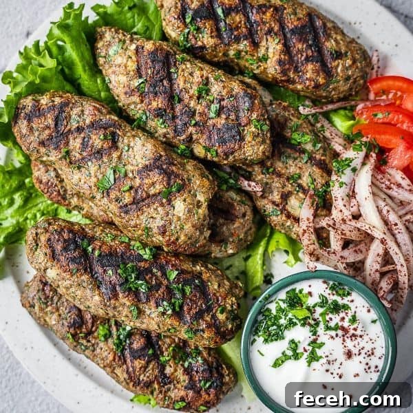 chicken kafta pieces on a plate with yogurt sauce, tomatoes and onions.