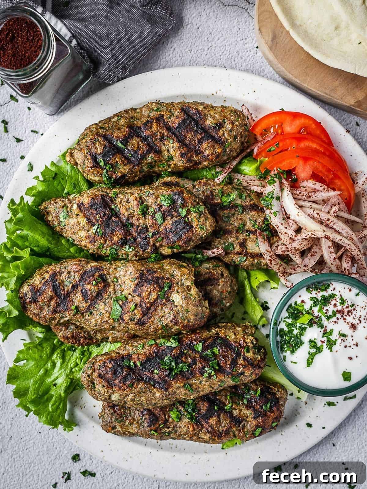 chicken kafta pieces on a plate with yogurt sauce, tomatoes and onions.