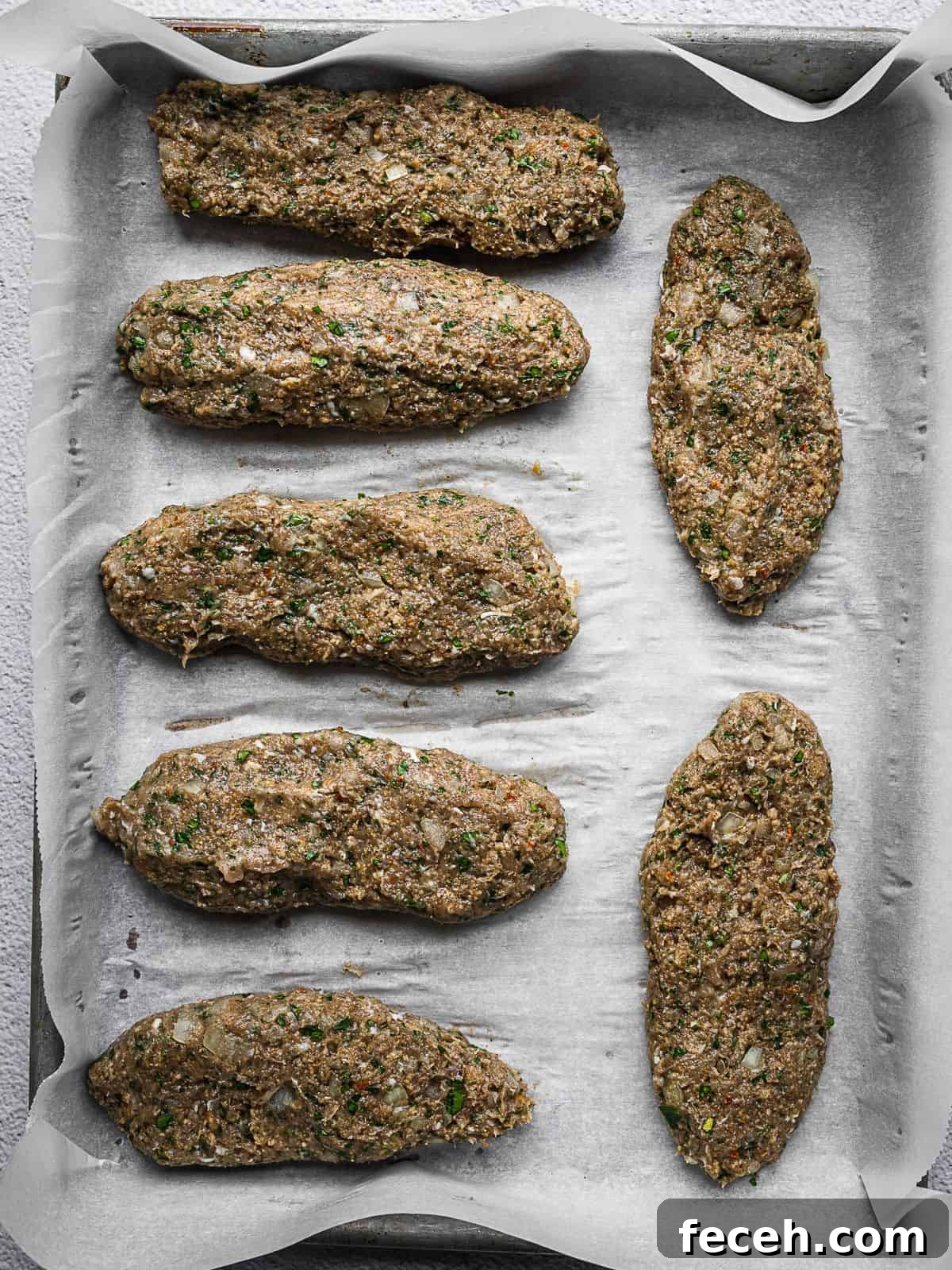 Chicken kafta formed into logs sitting on a baking sheet.
