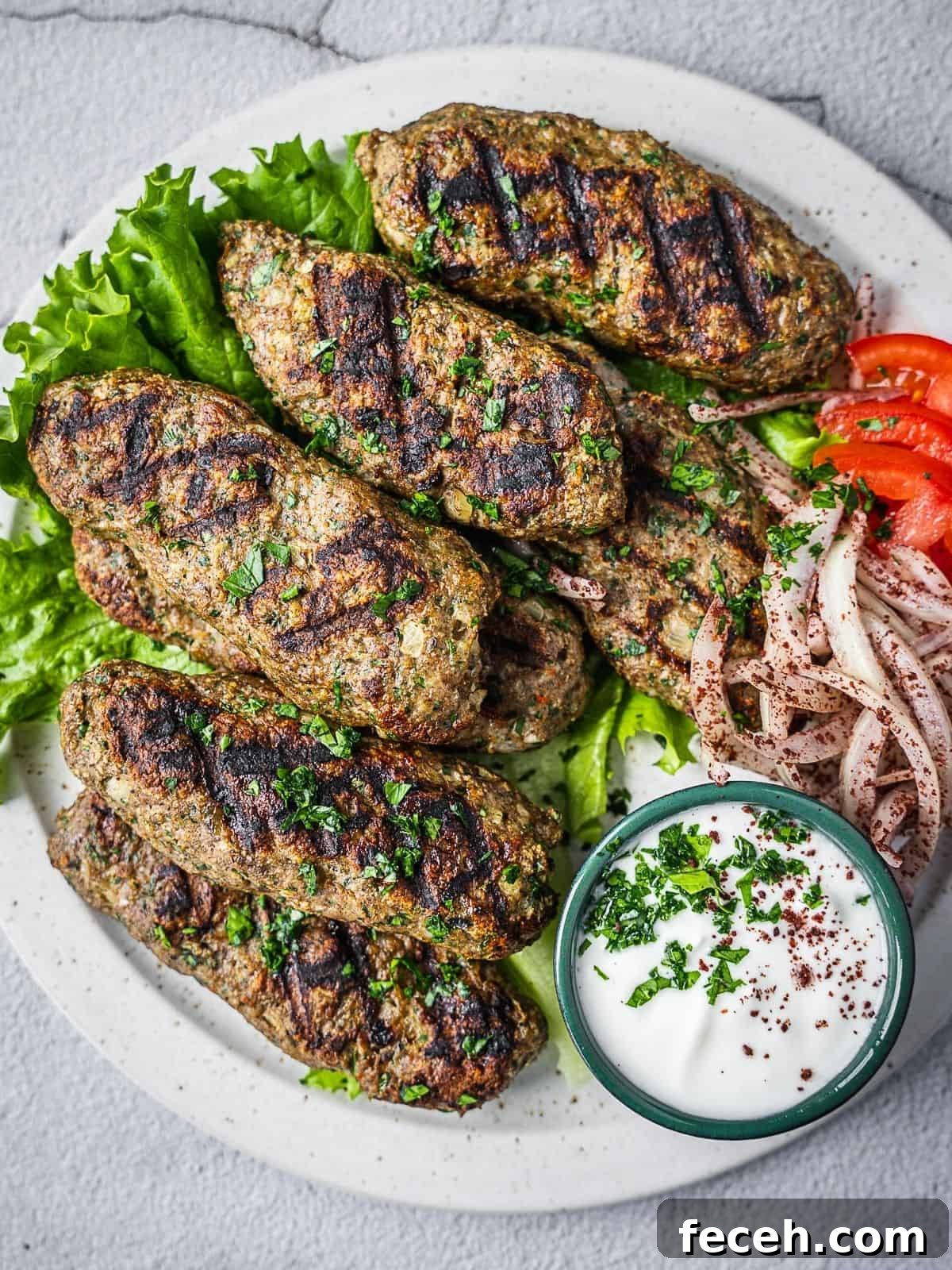 chicken kafta pieces on a plate with yogurt sauce, tomatoes and onions.