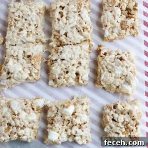 Golden Graham Rice Krispie Treats Recipe — Crispy Marshmallow Squares 7 squares of Rice Krispie treats on parchment paper with visible pieces of Golden Grahams and marshmallows